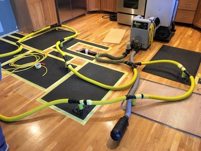 Hardwood floor drying system in operation Floor-drying mats and hoses connected to a drying unit on a hardwood floor