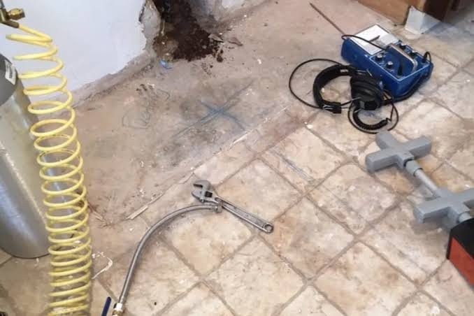 Locating a slab leak with acoustic equipment Acoustic leak detection equipment and headphones on a tile floor beside an opened wall